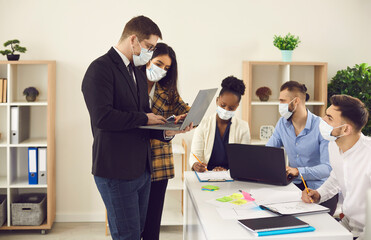 Office workers taking coronavirus precautions and preventive measures at work. Young multiethnic company employees all wearing face masks working on business project together during Covid 19 pandemic
