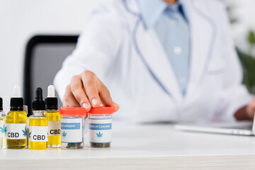 cropped view of blurred doctor reaching bottles with medical cannabis and cbd lettering on table
