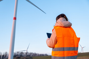 Engineer does maintenance and repairs wind wills or wind turbine using a tablet in the orange vesta.