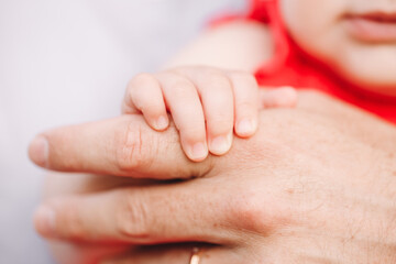 Closeup of baby fingers holding father parent hand palm. Baby trust and confidence in adult parent. Parent holding child daughter infant in arms. Authentic lifestyle parenting fatherhood moment.