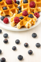 Naklejka premium Top view of waffles with raspberries and blueberries, on plate, selective focus, on white table with blueberries, in vertical