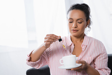 african american woman holding pipette with cbd liquid near cup of tea
