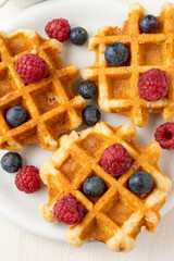 Aerial view of three waffles with raspberries and blueberries on white plate, selective focus, vertical