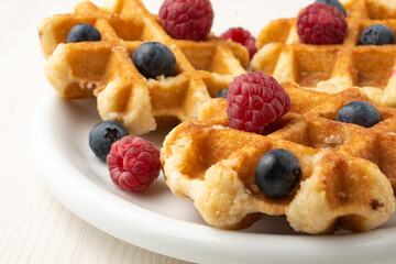 Top view of waffles with raspberries and blueberries on white plate, selective focus, horizontal