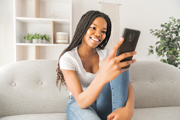 Young African American teen on a sofa in her living room using cellphone