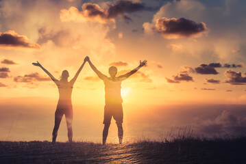 Maa and woman couple together with arms up to the sunset sky. Teamwork, strength, and feeling happy and motivated concept 