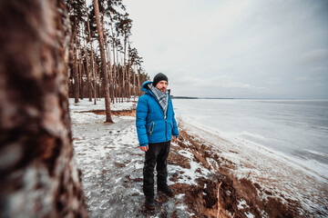 Icy cold a man standing in a blizzard near the forest is trying to keep warm. In a hat and a winter...