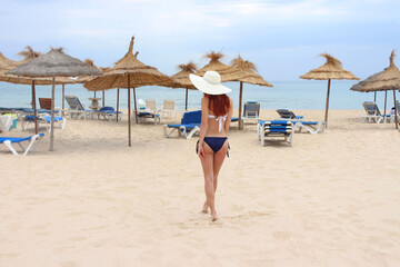Beautiful sexy young red-haired girl of European appearance in a swimsuit on a white beach in the summer.