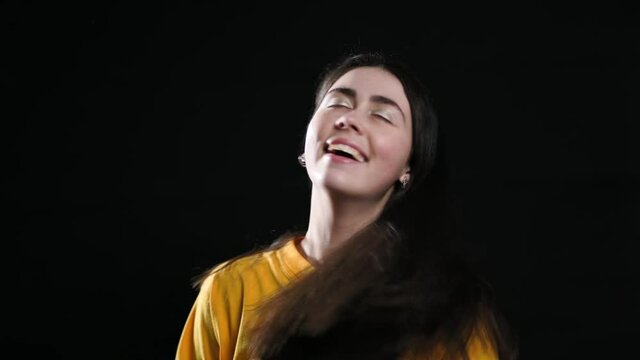 Portrait of a young woman shakes her head in different directions, showing her beautiful dark hair. Black background. Slow motion