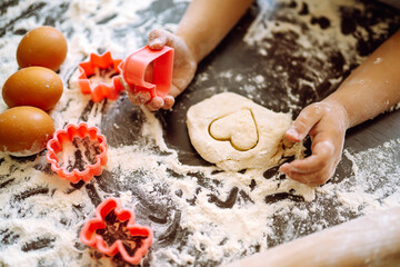 A little chef cutting out shapes heart and making ginger cookies. Close up of boy hands carving dough. Easter baking preparation. Children's art project, a craft for children.