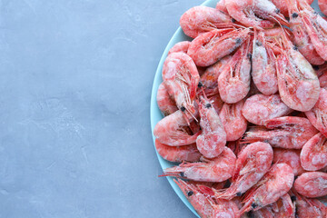 Pink frozen prawns on a blue platter on a gray concrete background with copy space. Top view.