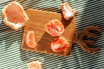 Fresh peeled grapefruit illuminated by sunlight on a wooden board