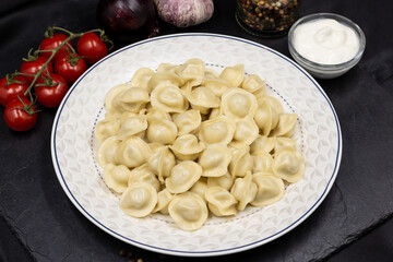 Russian small dumplings on a plate. Pelmeni. Black background.