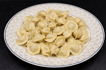 Russian small dumplings on a plate. Pelmeni. Black background.