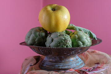 Apple and artichokes still life. Pink background. Metal antique bowl. Pictorial design.