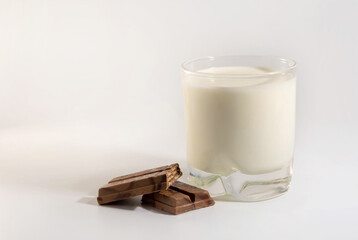 chocolate bar pieces and glass of milk on white background