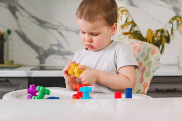 Child boy 2 y.o. plays with plastic colored shaped large screws and nuts, learning through the game.