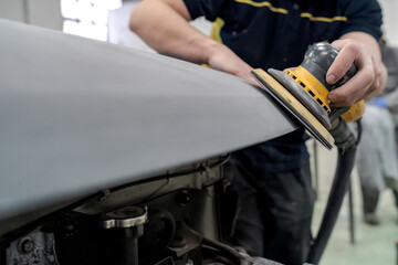 Crop anonymous male mechanic using machine for polishing car while preparing automobile for painting in workshop