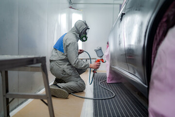 Side view of male in respiratory mask and protective suit painting car with spray gun in service