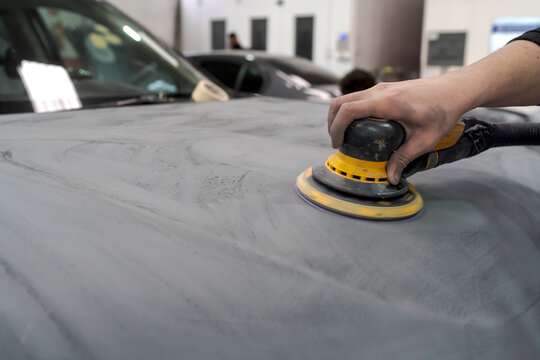 Crop anonymous male mechanic using machine for polishing car while preparing automobile for painting in workshop