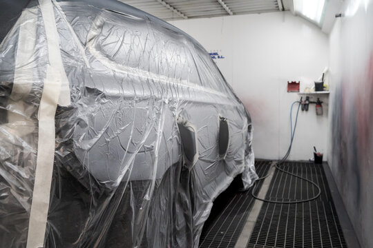 Modern automobile covered with plastic material prepared for painting and parked in car repair service center