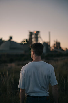 Back view of anonymous male on meadow against power station under gray sky in evening field
