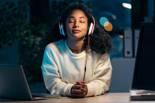 Confident african woman listening to music with earphones while relaxing of work in the office at home.