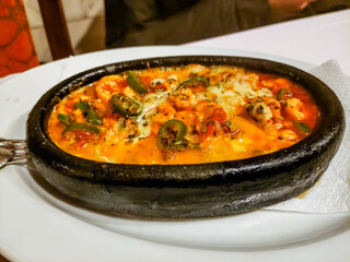 Baked fish with vegetables in a creamy sauce lies in a black frying pan