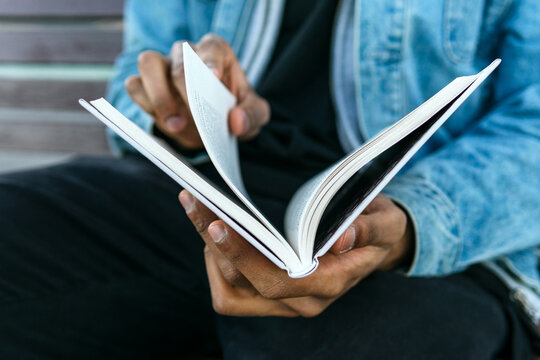 Cropped unrecognizable adult ethnic male in casual clothes reading journal while sitting on urban street