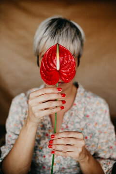 Unrecognizable female with manicure wearing dress demonstrating red laceleaf with pestle and green stem while standing in room on blurred background