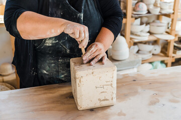 Crop anonymous female master in apron taking clay pot out of mould on table in pottery studio