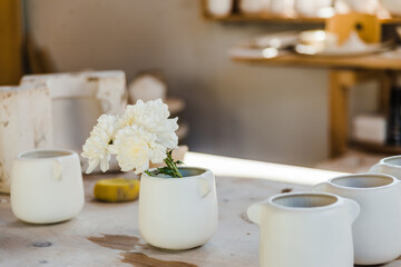 Set of white ceramic cups with flowers placed on counter in light studio near objects for handicraft