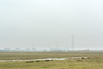 Fototapeta na wymiar Meadow with on the horizon electricity poles and new build houses under overcast sky.