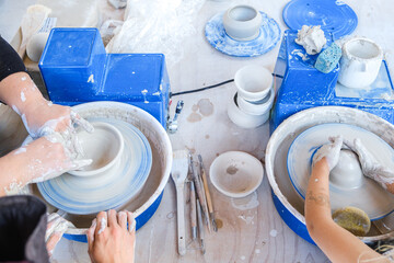 From above crop unrecognizable female standing near pottery wheel while shaping clay pot with little girl in light workshop