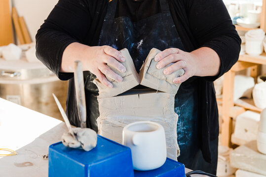 Crop unrecognizable female artisan in apron cutting clay while preparing for sculpturing in workshop