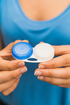 High angle crop anonymous female in blue shirt showing plastic pack of contact lenses