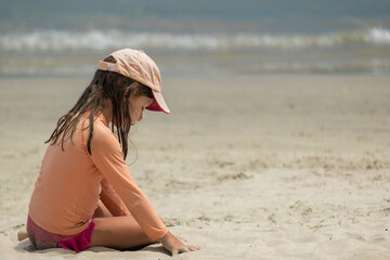 little girl playing alone sitting on the beach sand