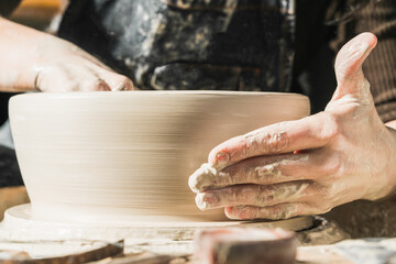 Cropped anonymous female artisan using pottery wheel and creating handmade earthenware in workshop