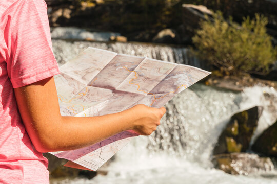 Unrecognizable traveling woman standing with paper map near waterfall in Ordesa y Monte Perdido National Park and orientating during vacation in Pyrenees mountains