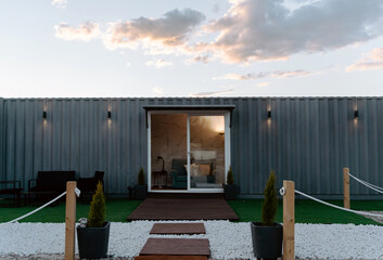 Modern gray shipping container house with glass doors located on grassy meadow and decorated with lush potted plants