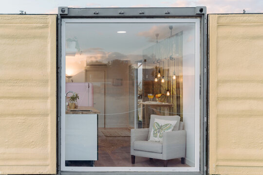 Small Stylish Kitchen And Comfy Armchair Behind Glass Wall Of Contemporary Container House In Daylight