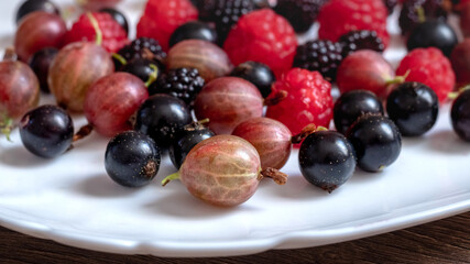 Assorted berries of raspberries, gooseberries, currants on a white plate