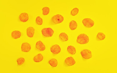 Potato crisps orange from paprika flavouring arranged on yellow board, view from above