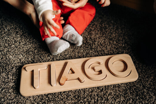 Cropped unrecognizable little baby playing on floor with wooden toy with Tiago name letters