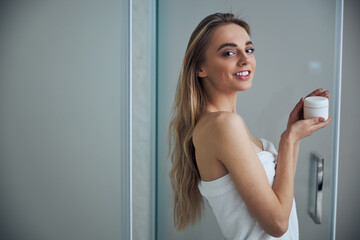 Contented long-haired female holding a face cream in her hands