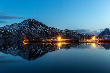 Scenic view of wooden piers in harbor with illuminated lamps located near sea in mountainous terrain in evening in Norway