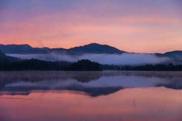 Scenic view of lake with smooth surface located in mountainous terrain under sunset sky in Norway