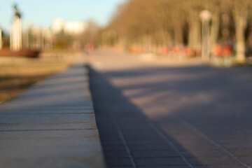 Spring in the city, the sunlit empty street paved with stone next to the park. Close-up view from sidewalk level