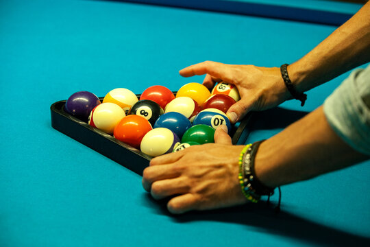 Crop male with curly hair making pyramid of balls for starting play billiards