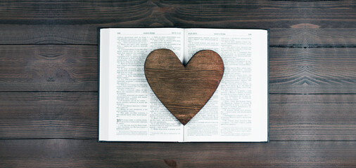 The open book is the holy bible. Scripture. Heart. Love. Prayer. On a wooden table.